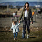 A woman and a child walking on a beach. The woman is wearing a freedom leg brace