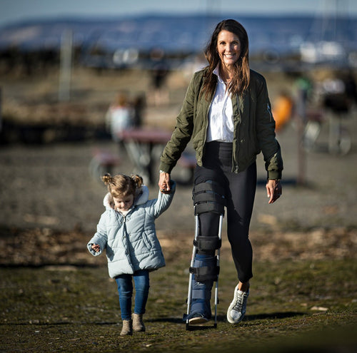 A woman and a child walking on a beach. The woman is wearing a freedom leg brace