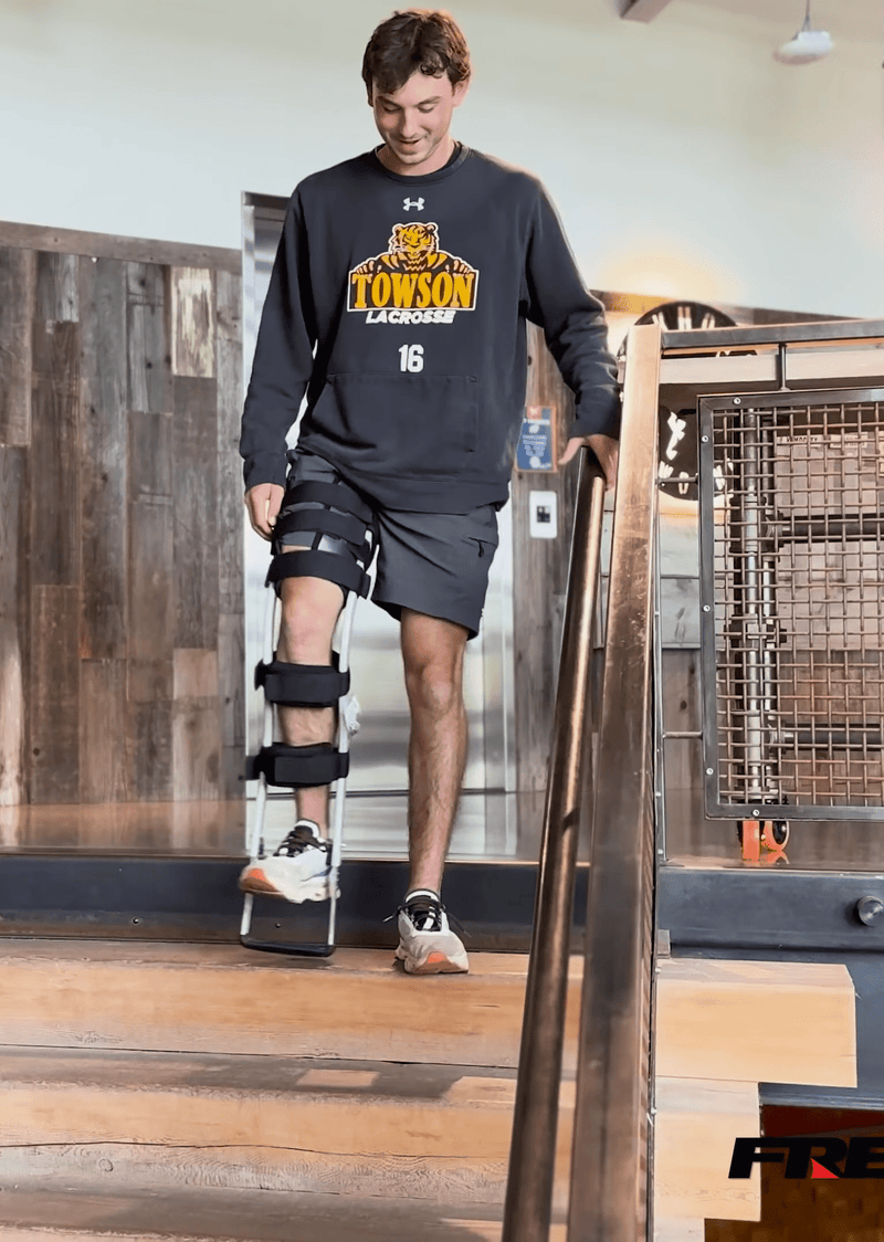 Person wearing Freedom leg brace safely walking down stairs holding onto a handrail